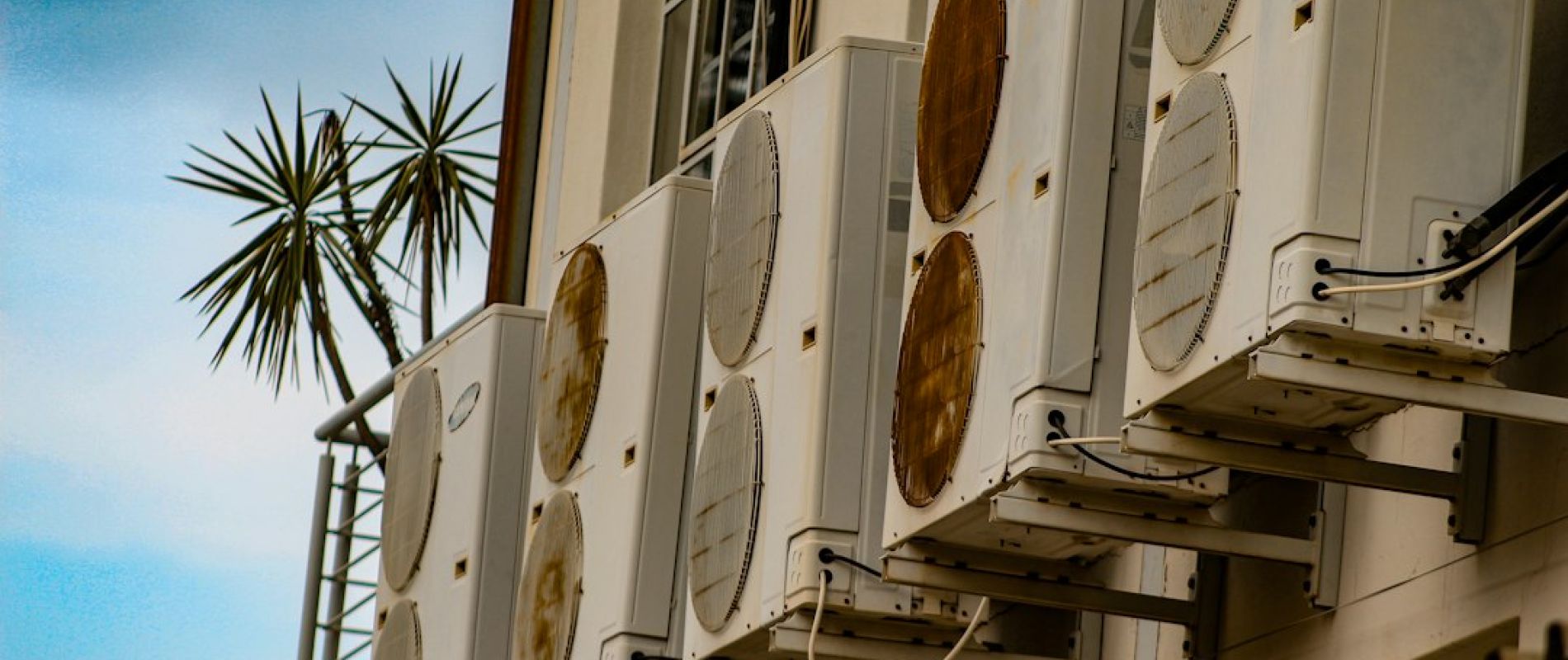 Unidades exteriores de aire acondicionado instaladas en fachada de edificio con palmeras y cielo azul