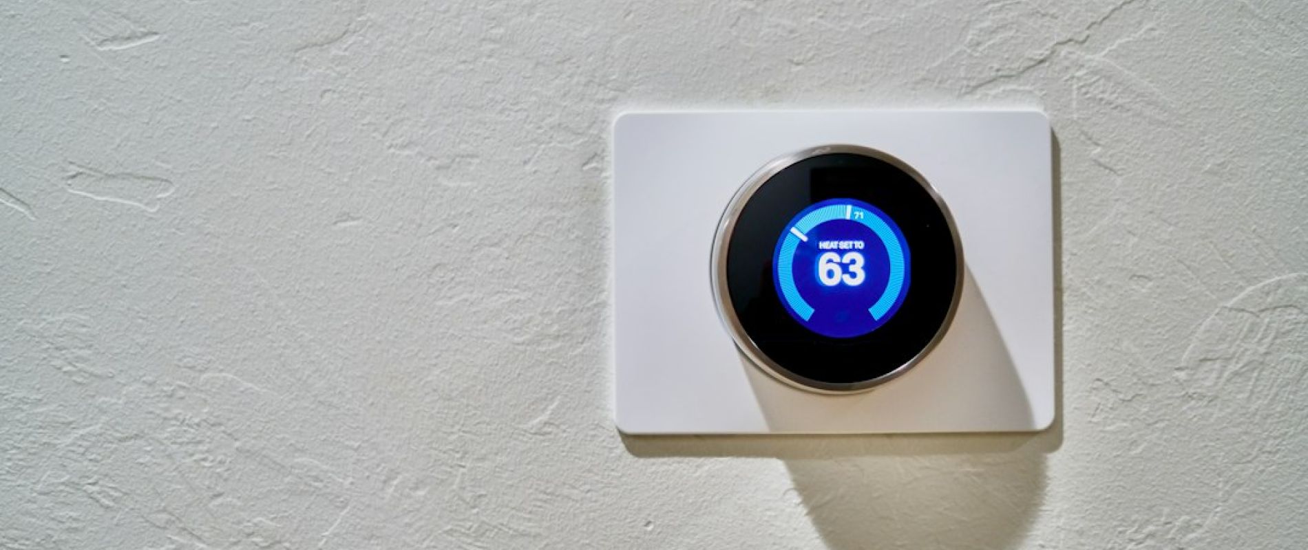 Termostato inteligente con pantalla digital azul mostrando temperatura de 63 grados en pared blanca