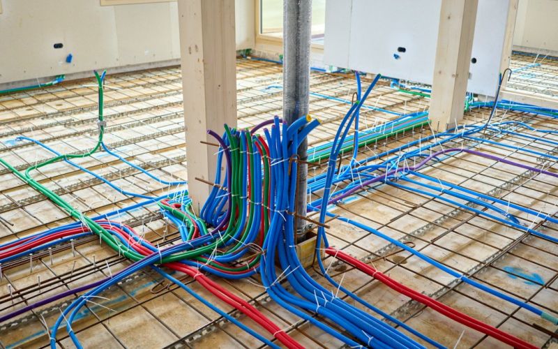 Instalación de tuberías de suelo radiante con mangueras azules, rojas y verdes sobre malla metálica en construcción
